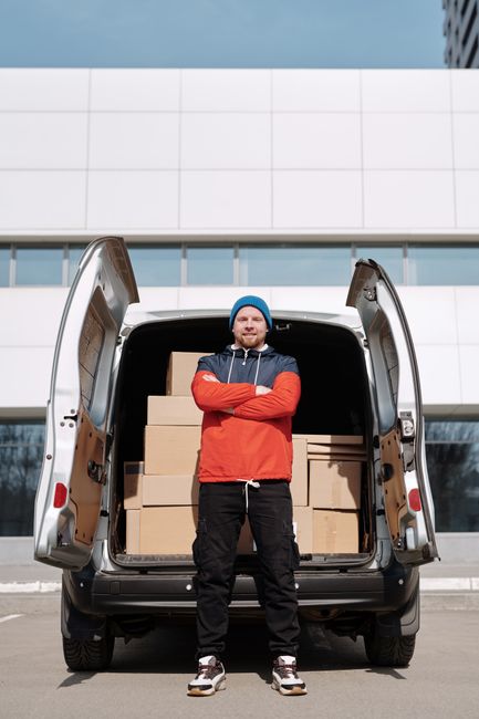Two movers from Man with Van Hammersmith are engaged in a home relocation process, transferring a large, dark green piece of furniture covered with a protective fabric blanket into the back of a black