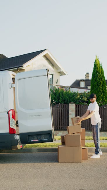 A man wearing a white polo shirt and cap is seen standing outside the back of a vehicle, likely a van used for home relocation, during the late afternoon or early evening with the sun setting in the b